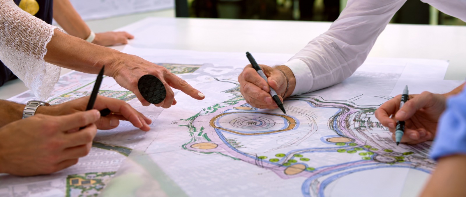 Progettisti al tavolo da disegno con planimetrie a colori di un parco e di un giardino